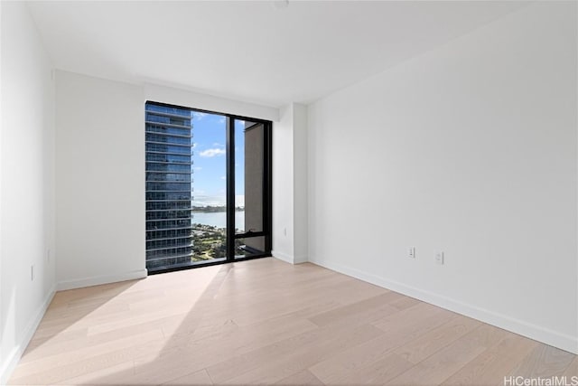 empty room with a water view, light wood-style floors, and baseboards