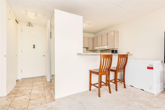 411 Hobron Ln Unit 703, Honolulu, HI 96815 - kitchen with under cabinet range hood, fridge, light countertops, a breakfast bar area, and cream cabinetry