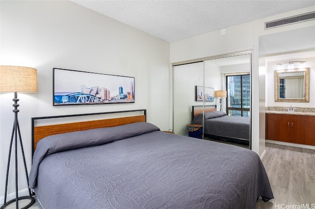 bedroom with a textured ceiling, sink, connected bathroom, light hardwood / wood-style floors, and a closet