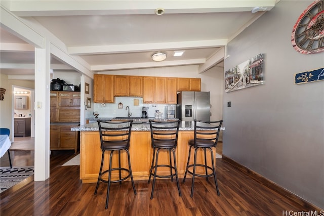 kitchen featuring lofted ceiling with beams, stainless steel fridge with ice dispenser, a kitchen breakfast bar, dark hardwood / wood-style flooring, and decorative backsplash