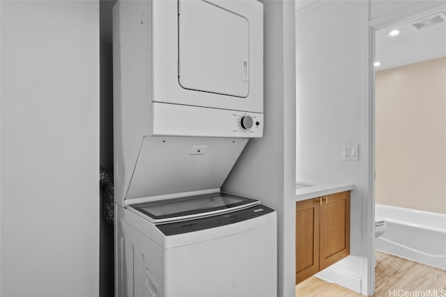 laundry room featuring stacked washer / drying machine and light hardwood / wood-style flooring