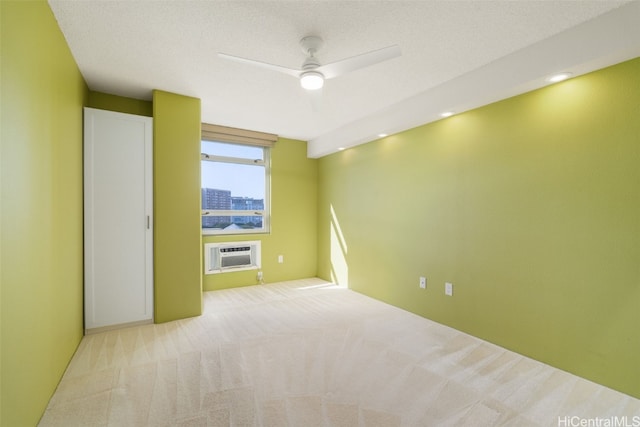 empty room with a wall mounted air conditioner, ceiling fan, light colored carpet, and a textured ceiling