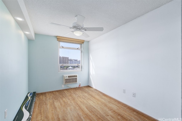 unfurnished room featuring an AC wall unit, ceiling fan, light hardwood / wood-style floors, and a textured ceiling