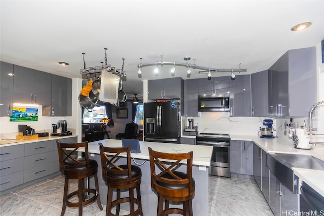 kitchen featuring a kitchen breakfast bar, backsplash, gray cabinetry, stainless steel appliances, and sink