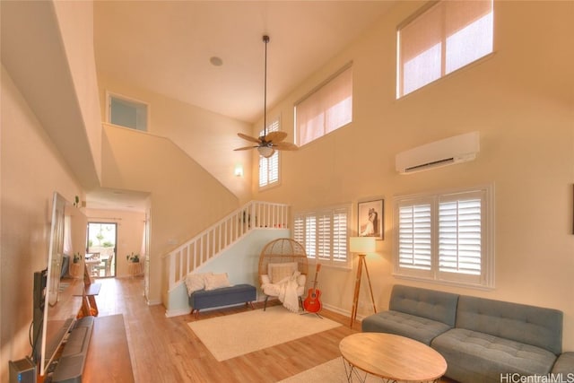 living room featuring a wall mounted air conditioner, ceiling fan, light wood-type flooring, and a towering ceiling