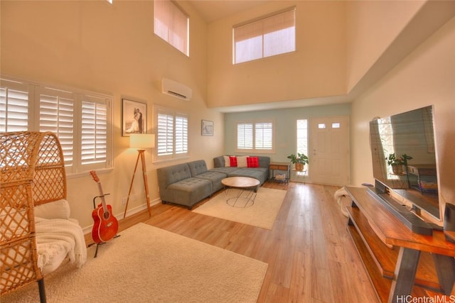 living room with a towering ceiling, a wall unit AC, and light hardwood / wood-style flooring