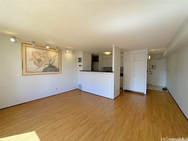 unfurnished living room with a textured ceiling and light hardwood / wood-style floors