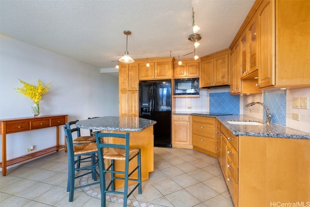 kitchen featuring sink, dark stone countertops, a breakfast bar area, a kitchen island, and black appliances