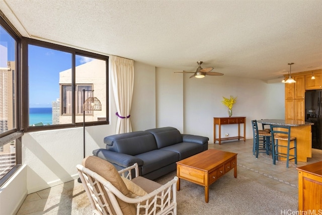 tiled living room featuring ceiling fan, a water view, and a textured ceiling