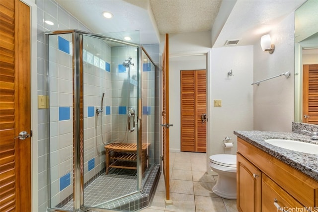 bathroom featuring vanity, a textured ceiling, a shower with door, tile patterned flooring, and toilet