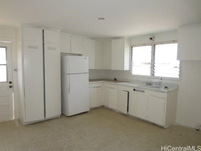 kitchen with white refrigerator, white cabinetry, and sink