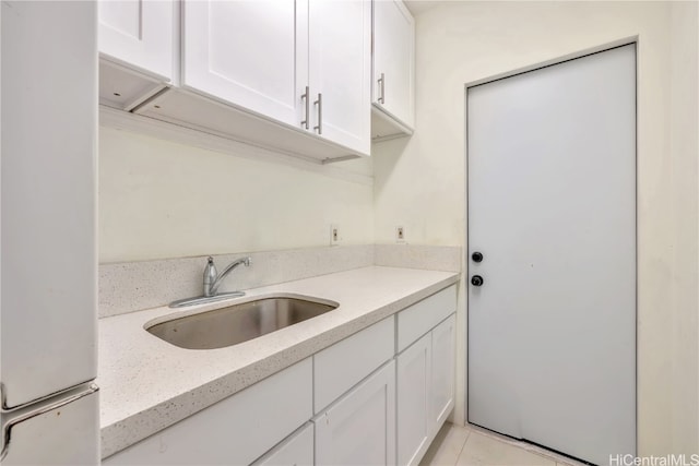 kitchen with light tile patterned floors, white refrigerator, white cabinetry, and sink