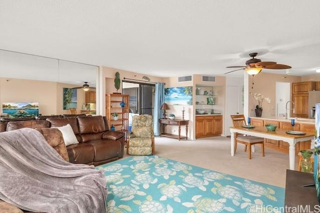 living area with ceiling fan, visible vents, and light colored carpet