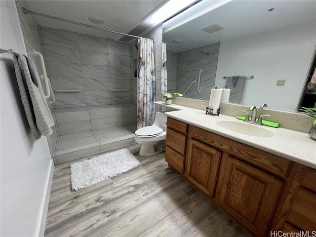 bathroom with visible vents, toilet, vanity, wood finished floors, and tiled shower