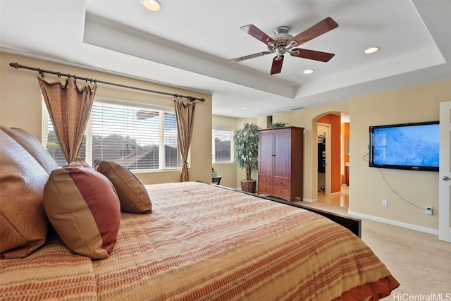 bedroom with ceiling fan, light carpet, and a tray ceiling