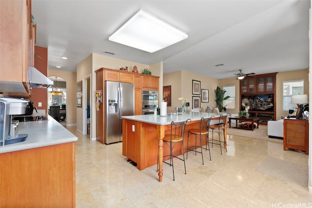 kitchen with a breakfast bar area, ceiling fan, a kitchen island, stainless steel appliances, and extractor fan