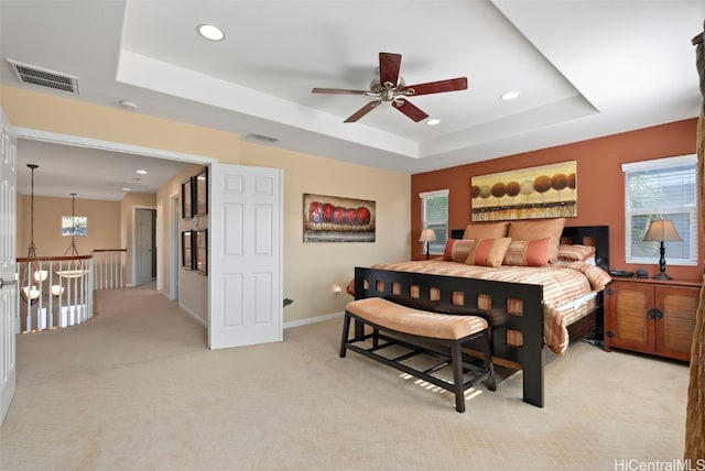 carpeted bedroom with a raised ceiling and ceiling fan