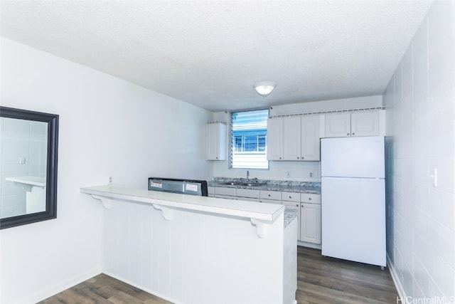 kitchen with a breakfast bar, white cabinetry, white fridge, dark hardwood / wood-style flooring, and kitchen peninsula