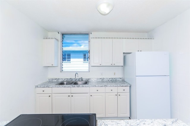 kitchen with a textured ceiling, sink, range, white fridge, and white cabinetry