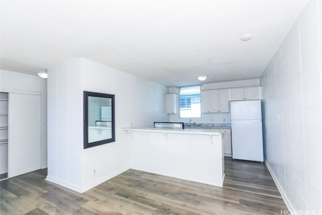 kitchen featuring white refrigerator, dark hardwood / wood-style flooring, white cabinetry, a kitchen bar, and kitchen peninsula