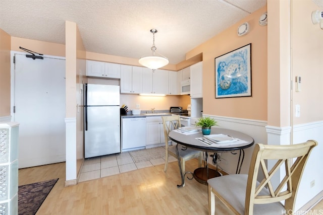 kitchen featuring sink, light hardwood / wood-style floors, decorative light fixtures, white appliances, and white cabinets