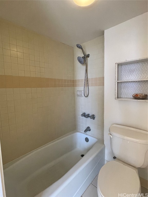 bathroom featuring tile patterned flooring, tiled shower / bath combo, and toilet