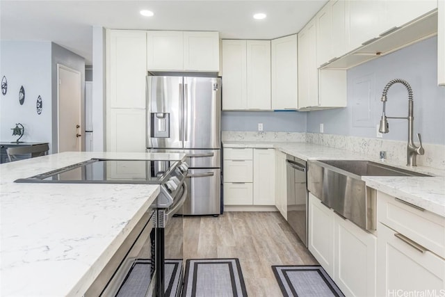 kitchen with white cabinetry, sink, light stone counters, appliances with stainless steel finishes, and light wood-type flooring