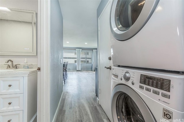 clothes washing area with laundry area, a sink, baseboards, light wood-style floors, and stacked washing maching and dryer