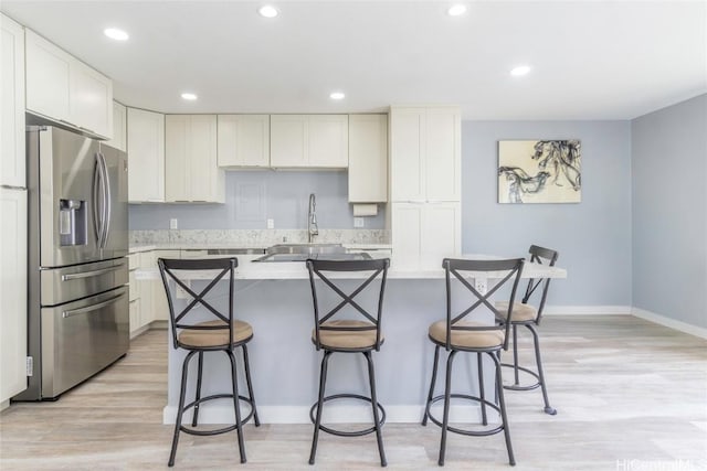 kitchen with light countertops, a kitchen island, stainless steel fridge, and light wood-style floors