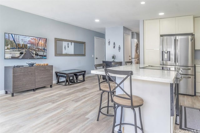 kitchen featuring stainless steel fridge, a kitchen breakfast bar, light stone countertops, light wood-type flooring, and stacked washing maching and dryer