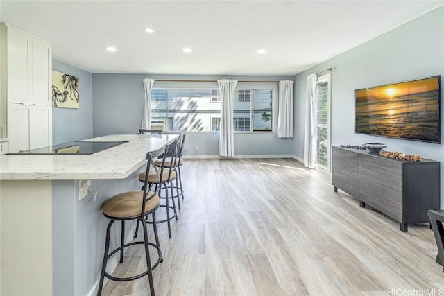 kitchen featuring a wealth of natural light, white cabinetry, light stone counters, light hardwood / wood-style flooring, and a breakfast bar area