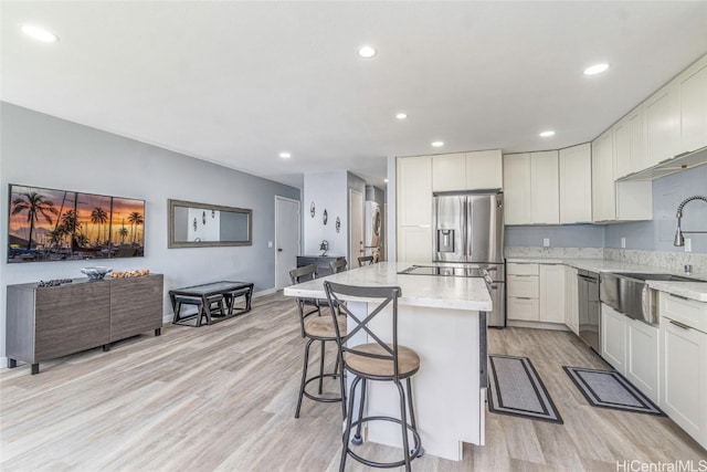 kitchen with a breakfast bar area, a sink, appliances with stainless steel finishes, light wood-type flooring, and a center island