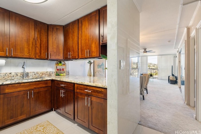 kitchen with ceiling fan, sink, light stone counters, backsplash, and light colored carpet