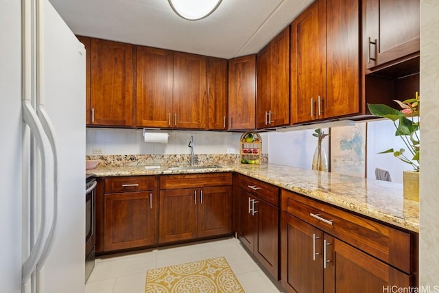 kitchen with white refrigerator, sink, stainless steel stove, light stone countertops, and light tile patterned flooring