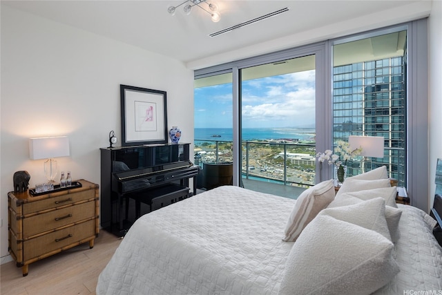 bedroom with access to exterior, a water view, visible vents, and light wood-type flooring