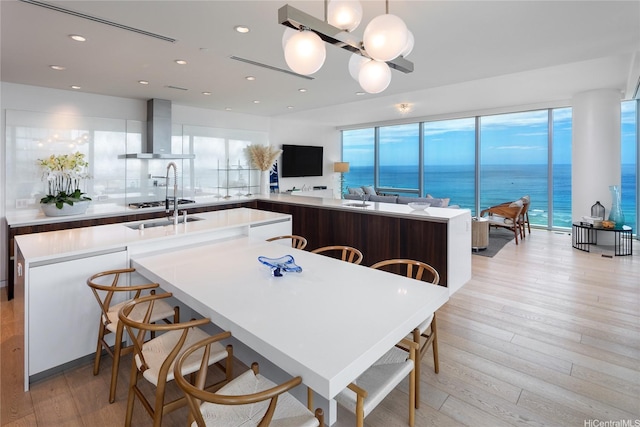 kitchen with wall chimney exhaust hood, light wood finished floors, recessed lighting, and light countertops