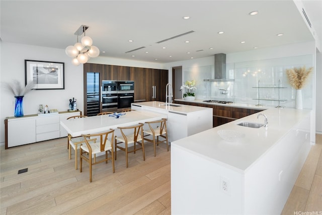 kitchen with light wood finished floors, stainless steel gas cooktop, a sink, modern cabinets, and wall chimney exhaust hood