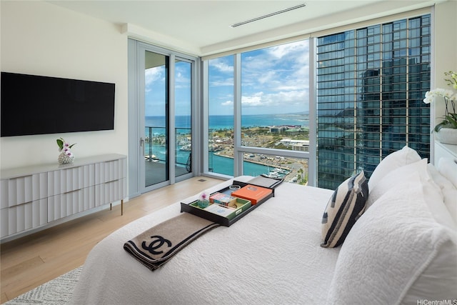bedroom with wood finished floors, a wall of windows, a water view, and access to exterior