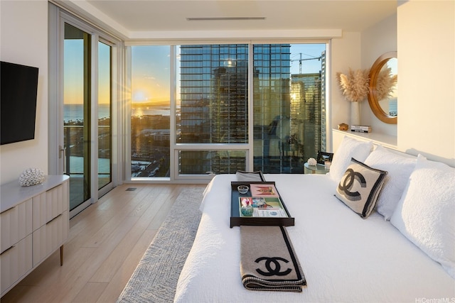 bedroom with hardwood / wood-style floors, access to outside, and a wall of windows
