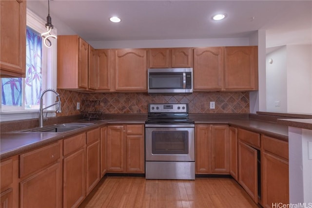 kitchen with pendant lighting, sink, tasteful backsplash, light hardwood / wood-style floors, and stainless steel appliances