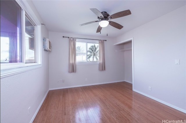 unfurnished bedroom with a wall mounted AC, hardwood / wood-style floors, a closet, and ceiling fan