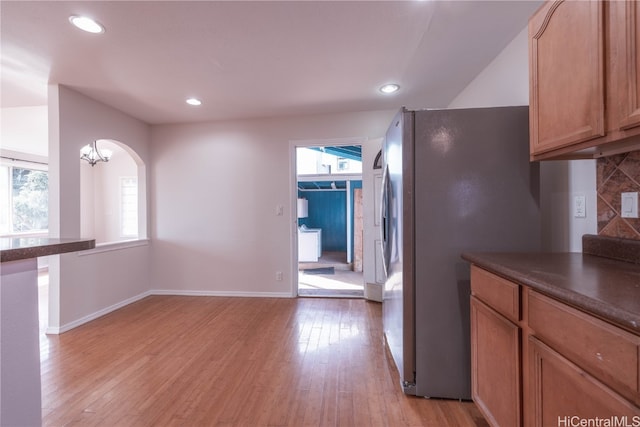 kitchen with decorative backsplash, light wood-type flooring, stainless steel refrigerator, and a wealth of natural light