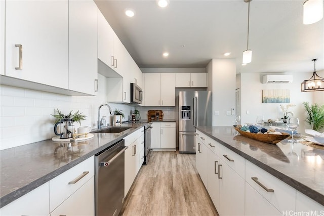 kitchen featuring white cabinets, an AC wall unit, hanging light fixtures, sink, and appliances with stainless steel finishes