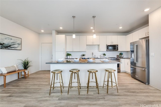 kitchen featuring appliances with stainless steel finishes, light wood-type flooring, pendant lighting, white cabinets, and a center island