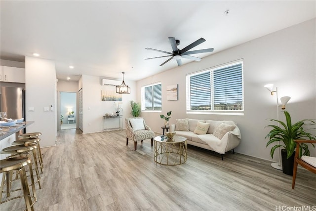 living room featuring light hardwood / wood-style flooring, ceiling fan with notable chandelier, and a wall mounted air conditioner