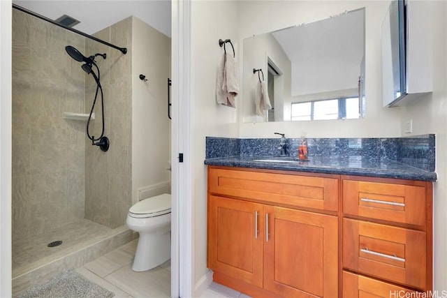 bathroom with tile patterned flooring, vanity, toilet, and a tile shower