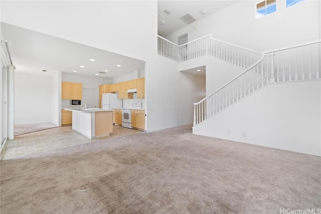 unfurnished living room featuring a high ceiling, light colored carpet, and sink