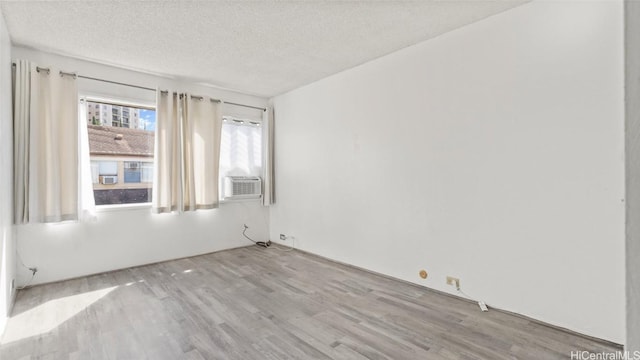 unfurnished room featuring light wood-type flooring, a textured ceiling, and cooling unit