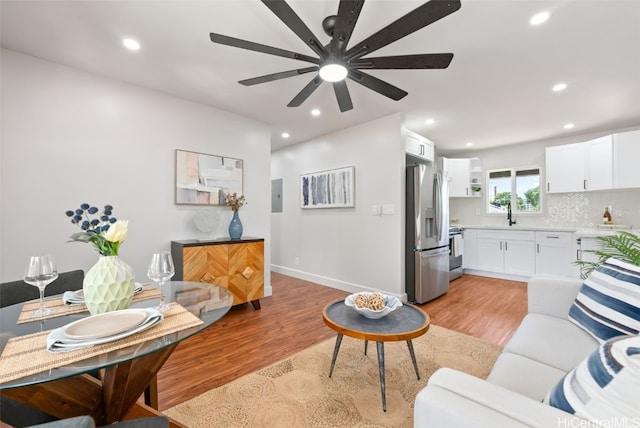 living room with electric panel, ceiling fan, sink, and light hardwood / wood-style floors