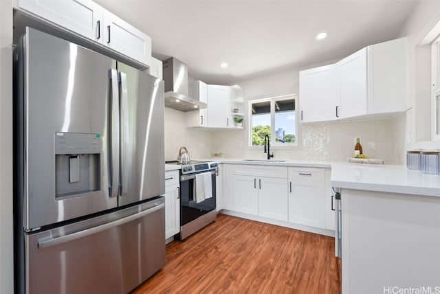 kitchen featuring stainless steel appliances, wall chimney range hood, sink, wood-type flooring, and white cabinets